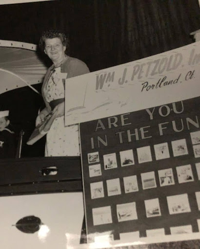 Agnes Petzold with Petzold’s Marine Center at a Connecticut boat show in the 1950s, smiling in front of a board of boats for sale.