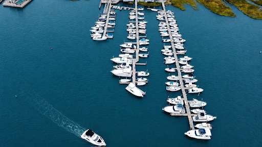 Aerial view of Petzold’s Port Clinton Marina in Clinton, Connecticut, with boats docked along multiple piers and a powerboat cruising through blue water.