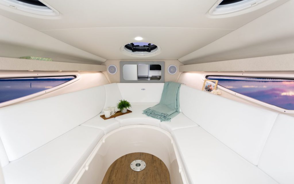 White upholstered bow seating in a freshly cleaned boat cabin, with a tray of mugs and a folded throw