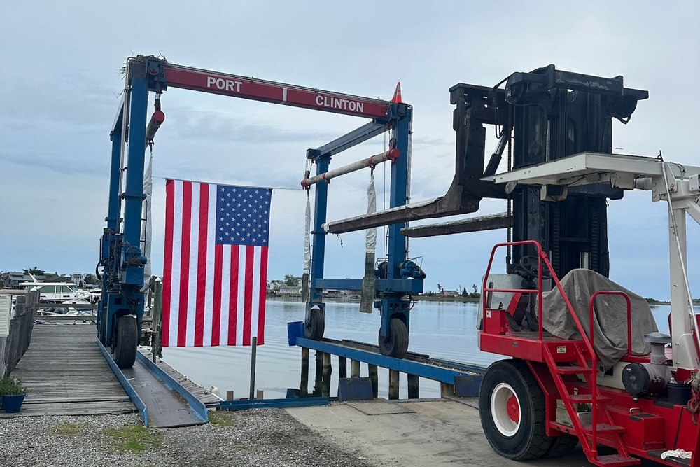 A large American flag hanging from the marina's travel lift over the water