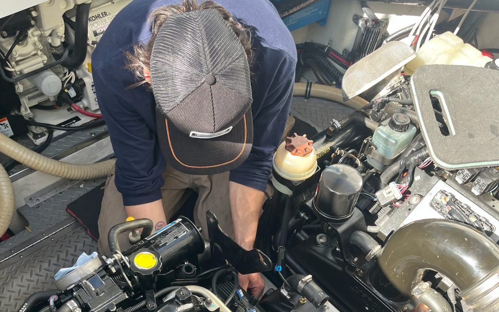 A marine technician leaning into a boat’s engine bay to service an inboard engine