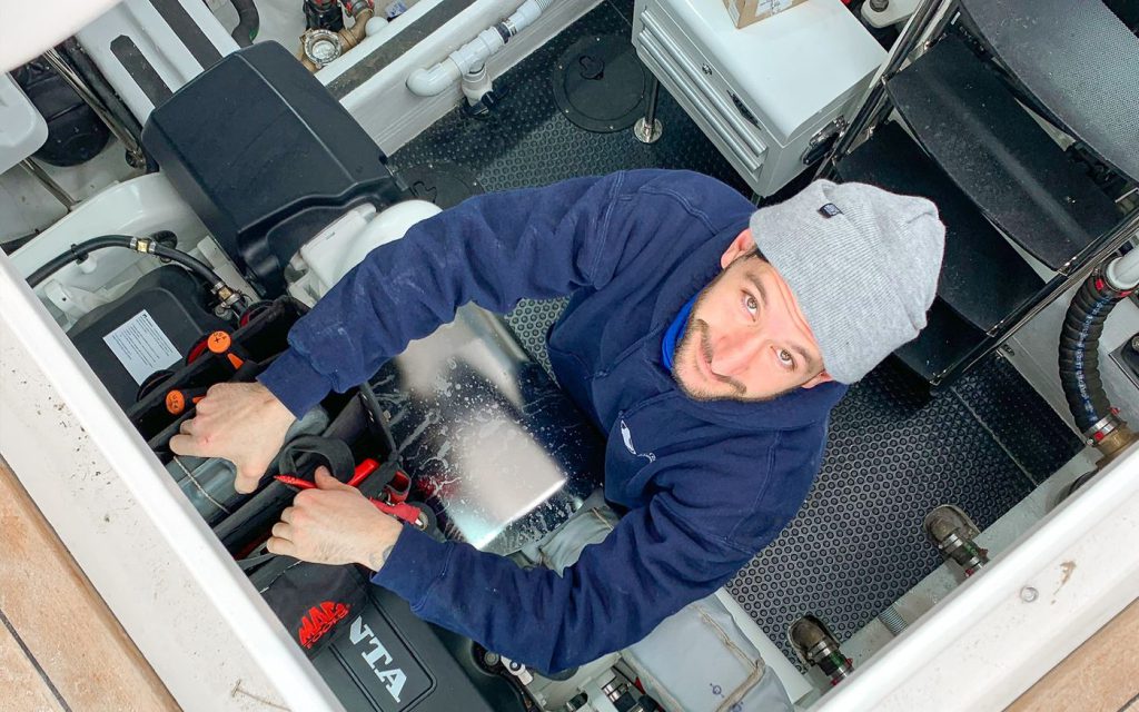 A marine technician working on an inboard engine inside a boat’s engine bay