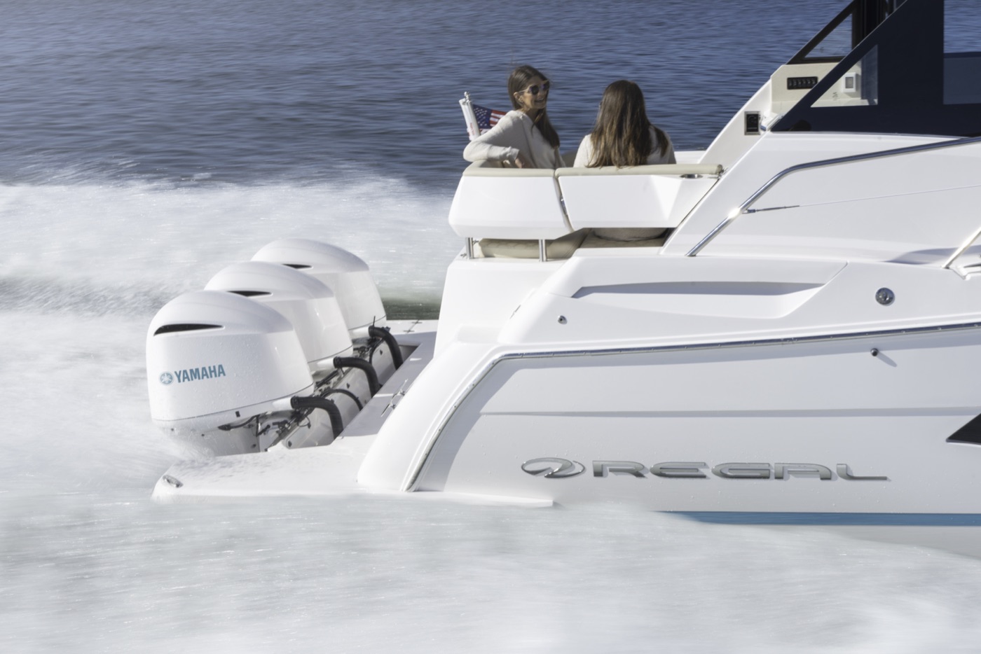 A Regal boat with a polished white fiberglass hull and triple Yamaha outboards underway