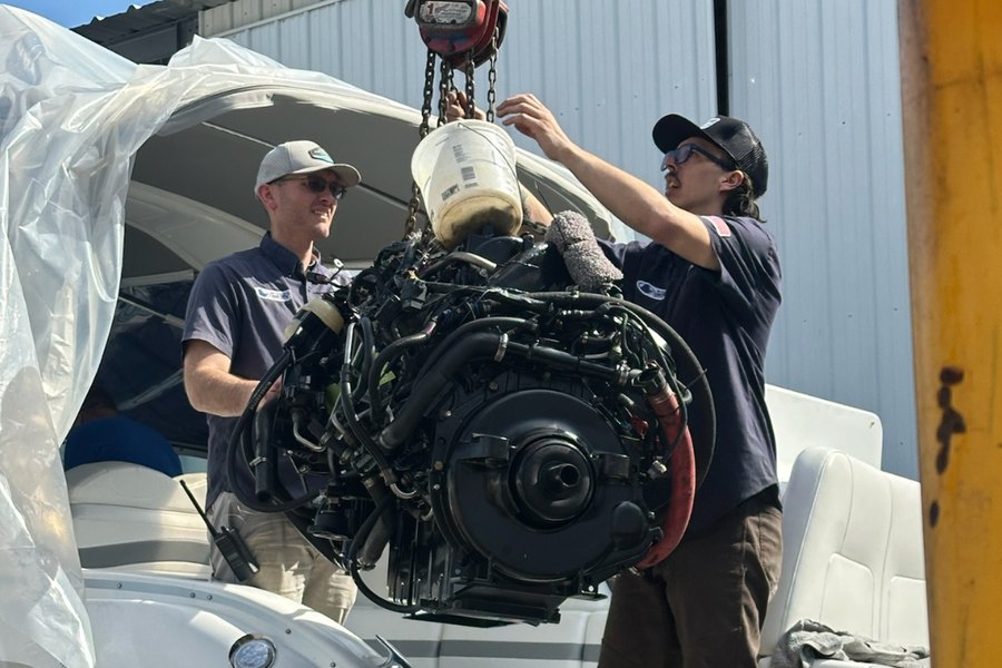 Two marine technicians lifting an engine out of a boat in the service yard